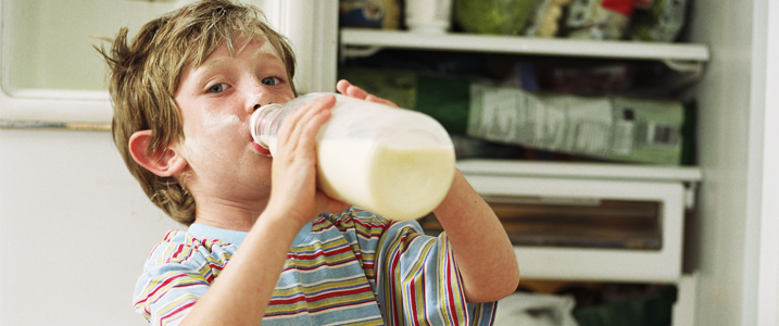 kid drinking milk in front of refrigerator